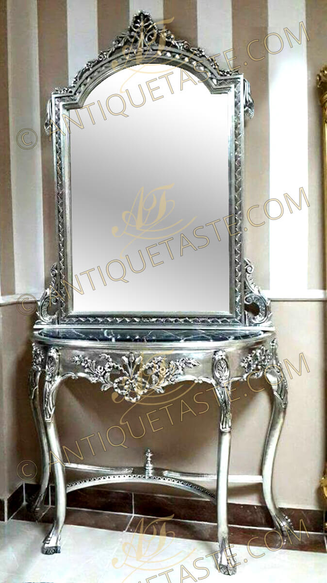 A fine Tiffany French silvered Rococo Louis xv style grand console with mirror, hand carved and silvered with French silver foils and applied with black patina, the domed top mirror crested with a seashell issuing blossoming garlands to the sides terminating with a pine cone pendants on a hammered background frame terminating with an acanthus c-scroll works resting on a D shaped black veined marble top. The D shape apron is ornamented with foliate and blossoming motifs and pierced center forming flowering ribbons. The cabriole splayed S shape legs are headed with foliate motifs terminating with claw and ball feet which is carved to represent a bird's claw grasping a ball derived from the Chinese dragon's claw holding a crystal ball or jewel and joined by a curvy sectional hammered X stretcher centered with a coned urn